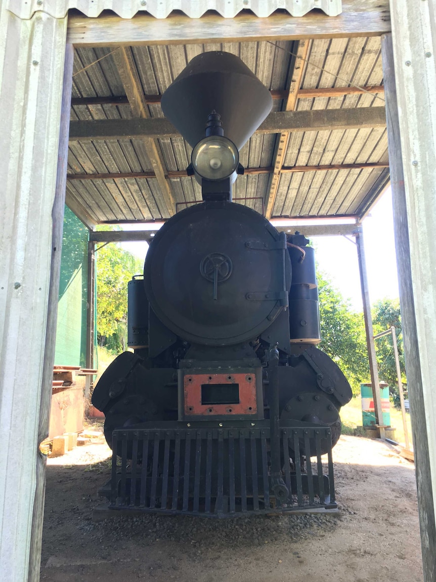 A small locomotive under a shed on a rural property.