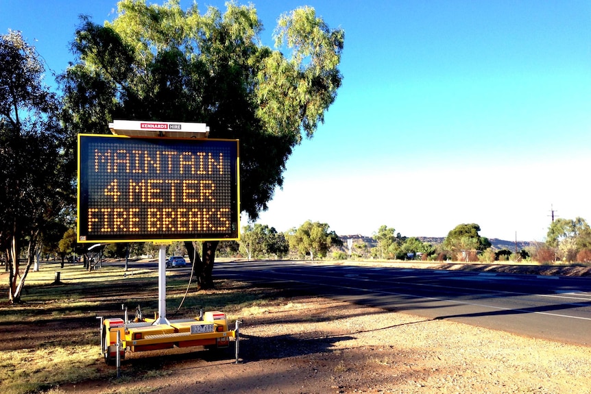 A fire warning sign reads "maintain 4 meter fire breaks" beside a road.