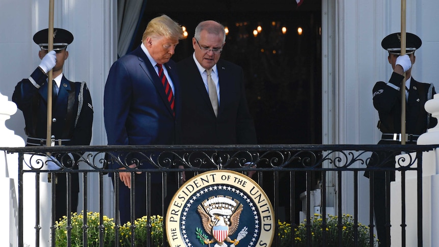 Donald Trump and Scott Morrison speak behind a fence emblazoned with the US presidential seal. Soldiers hold flags next to them.