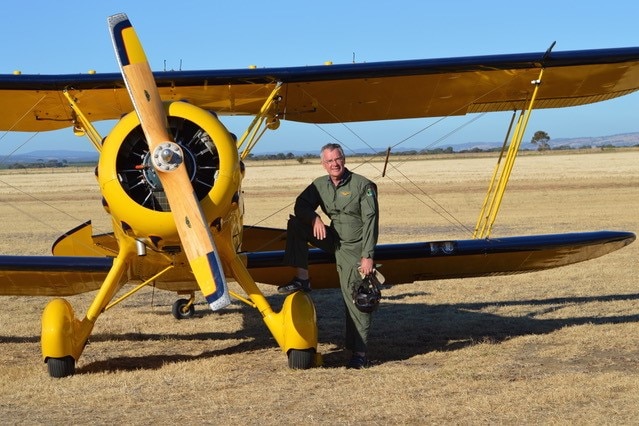 Pilot in khaki overalls standing outside yellow biplane