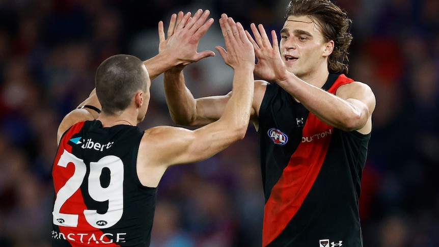Two AFL players engage in a high five with both hands, delighted after kicking a goal.