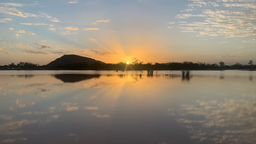 sunset over shallow lake of water, mountains and clouds reflected on the water surface