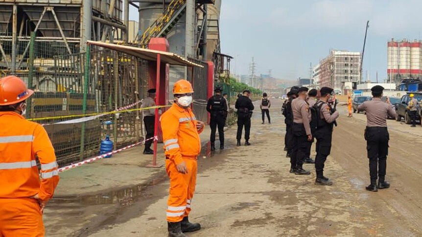Police officers and workers stand near the site where a furnace explosion occurred a