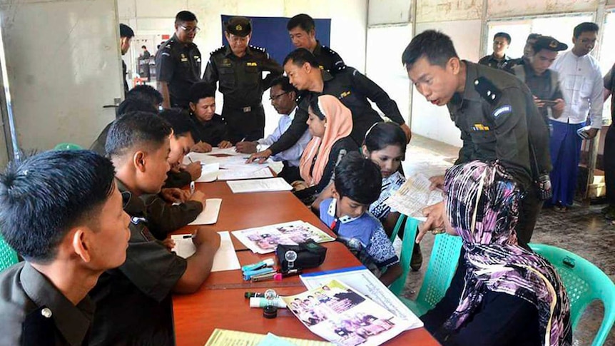 A Rohingya family of five talk with Myanmar immigration officials in a room.