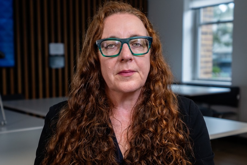 Un portrait basique de Carla Treloar regardant l'appareil photo avec une expression sérieuse et des lunettes à monture épaisse.