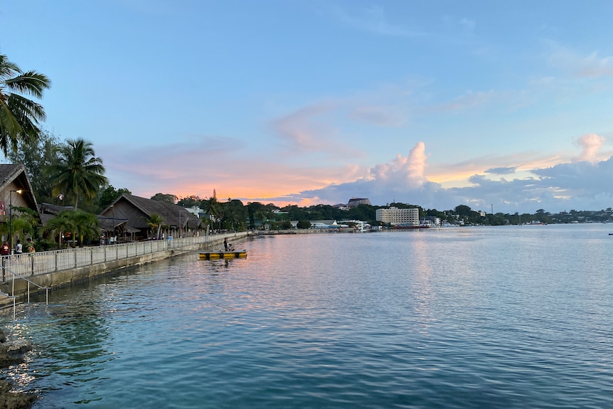 Sunset over Port Vila's seafront, with pink skies, and people looking over the water of Vila Bay.