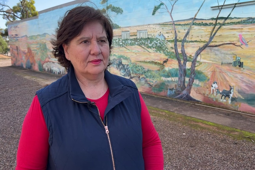 Woman with short brown hair standing in front of a mural depicting agricultural land.