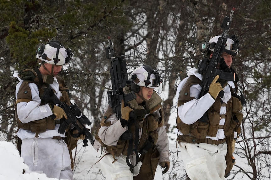 Three soldiers dressed in snow gear carry weapons.
