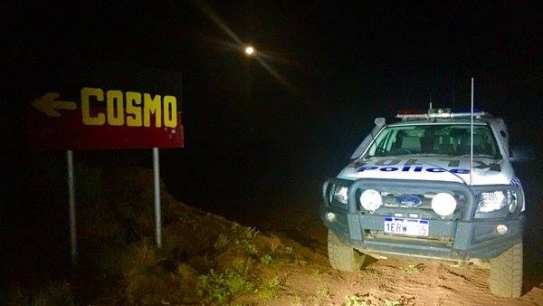 A police car parked next to a road sign on a remote highway.  