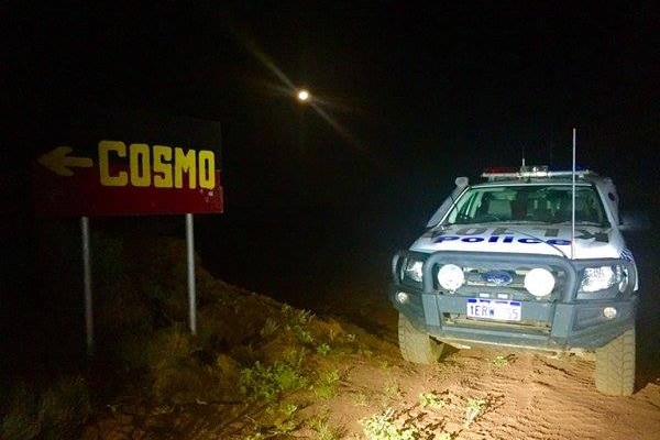 A police car parked next to a road sign on a remote highway.  