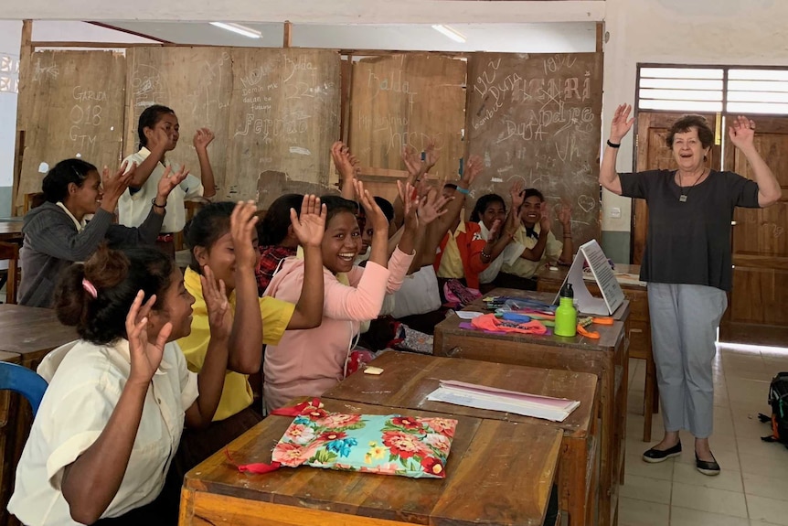 A classroom of Timorese children shake their hands to dry them after learning about washing their hands.