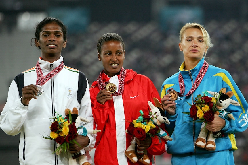 Three women line up and hold their medals while dressed in their country's tracksuits.
