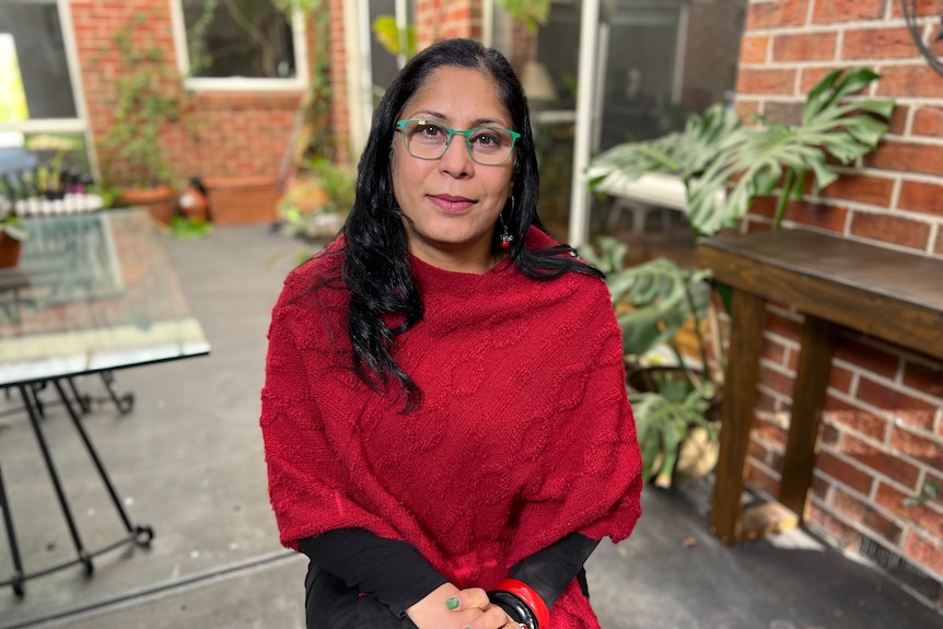 Manjula Shaw wearing a red top, seated calmly in a garden.