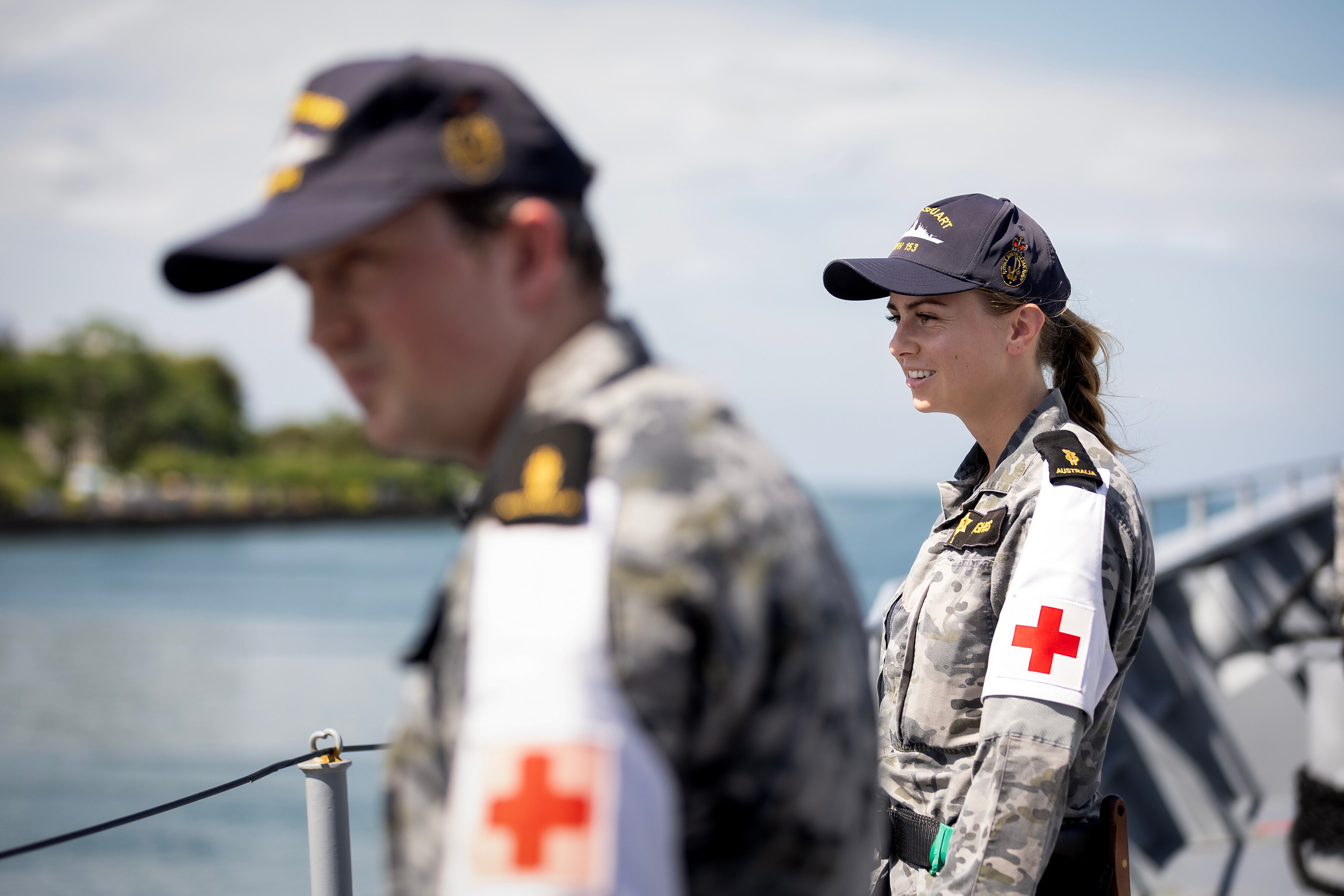 Two army personnel stand on a boat, looking out at the water.