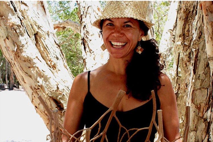 woman with straw hat smiling in front of a paperbark tree