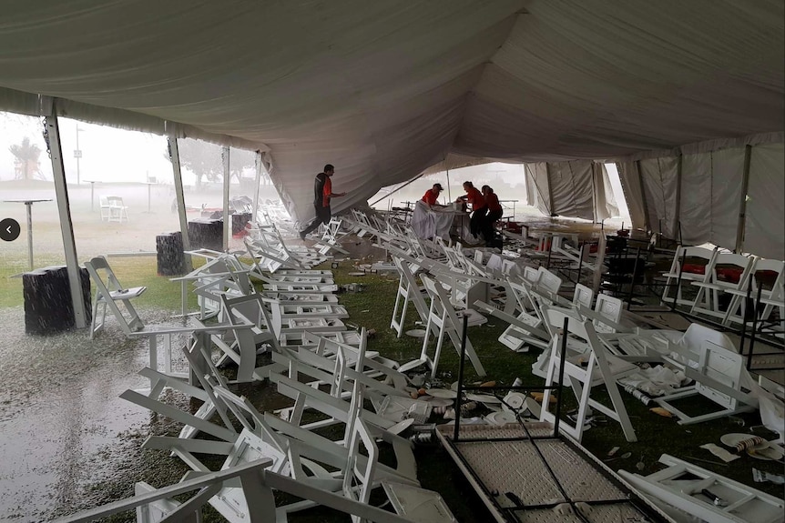 Plastic tables and chairs are flipped and a marquee falls after being smashed by rain.