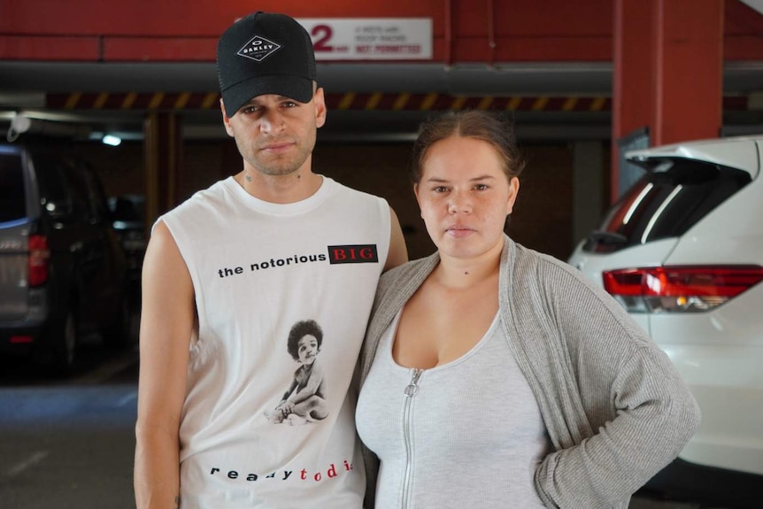 A young man and women pose for a photo in an underground carpark.