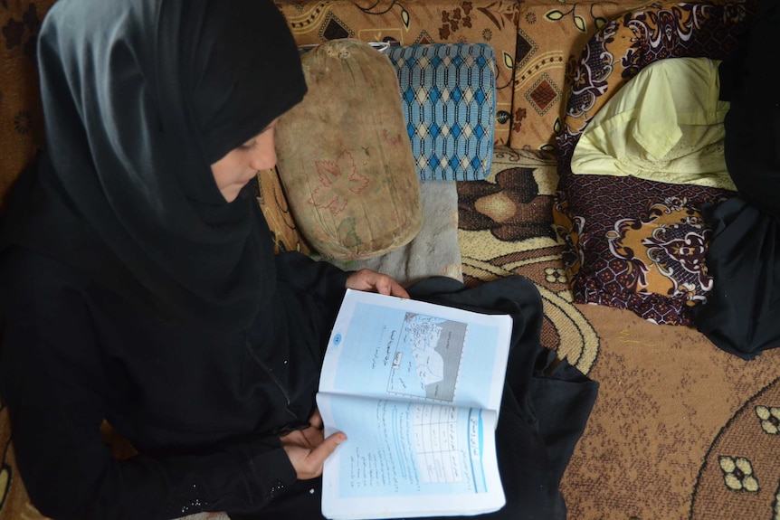 A young girl in a hijab reads a book