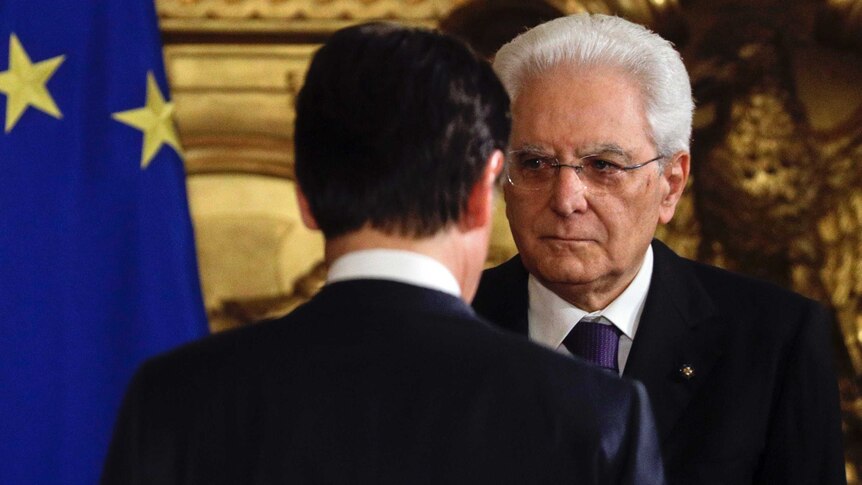 Italian President Sergio Mattarella is seen standing  in front of Premier Giuseppe Conte.