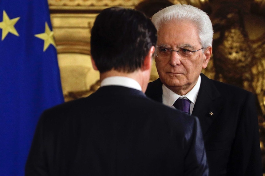 Italian President Sergio Mattarella is seen standing  in front of Premier Giuseppe Conte.