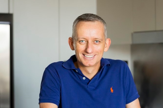 Singer David Valks standing in his kitchen. He's smiling and wearing a navy blue Polo shirt