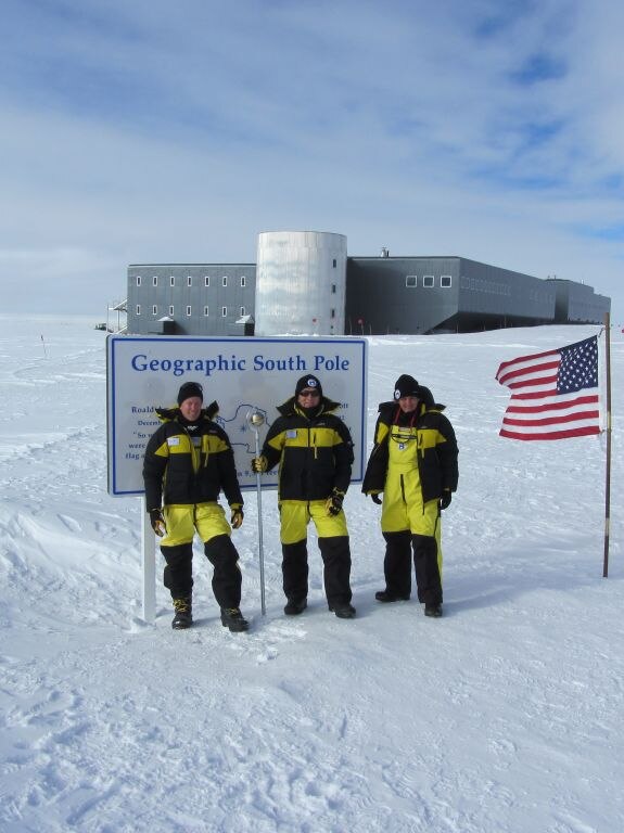 Three scientists standing in front of a sign at the South Pole