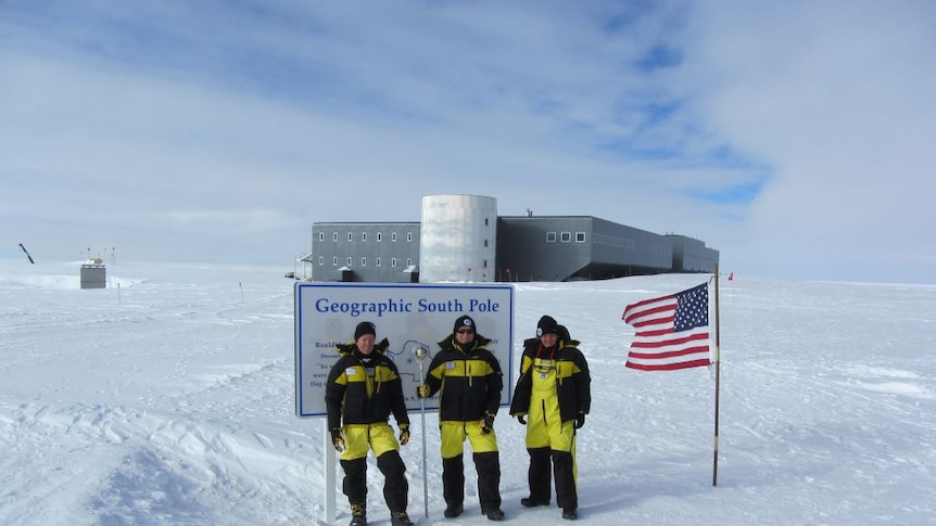 Three scientists standing in front of a sign at the South Pole