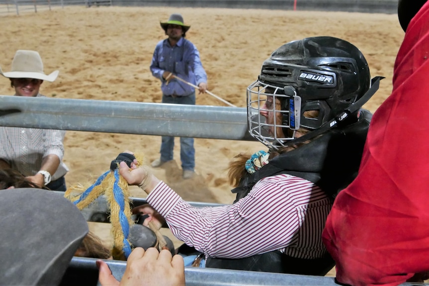 A woman wearing a helmet sits on a horse in a metal pen.