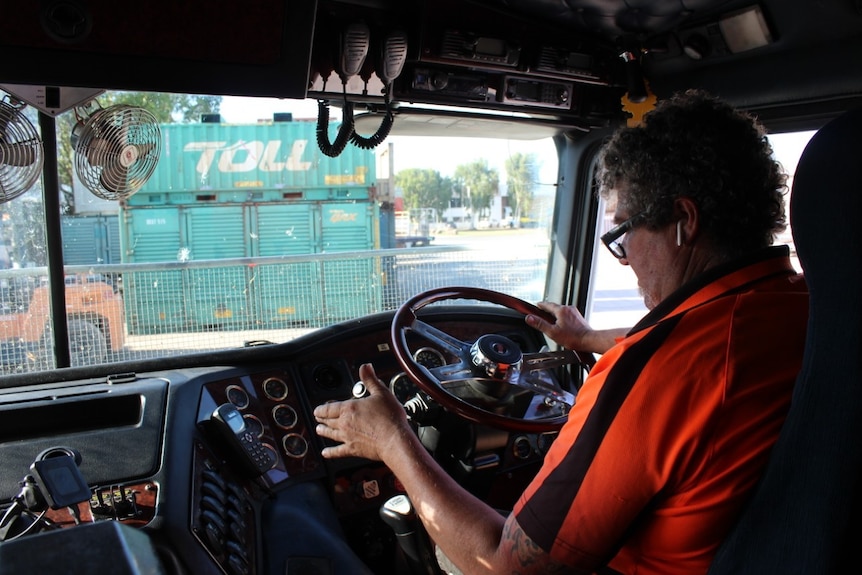 A man in a high vis shirt sits in the driver's seat of a truck.