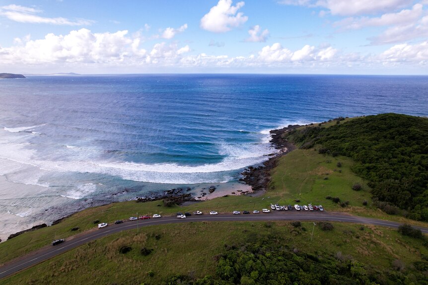 Aerial view of remote green grassy coastline overlooking ocean with a line of parked cars