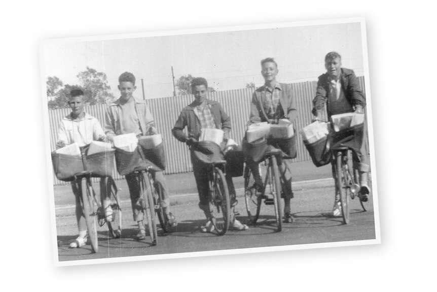 A group of boys standing on bikes in a line with newspapers in them.