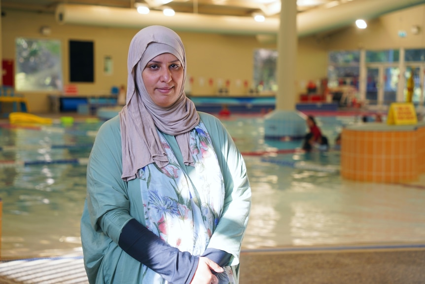 A woman wearing blue and beige garments stands by a swimming pool