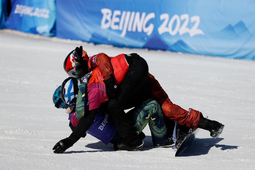 Three snowboarders are hugging, lying on top of each other. 