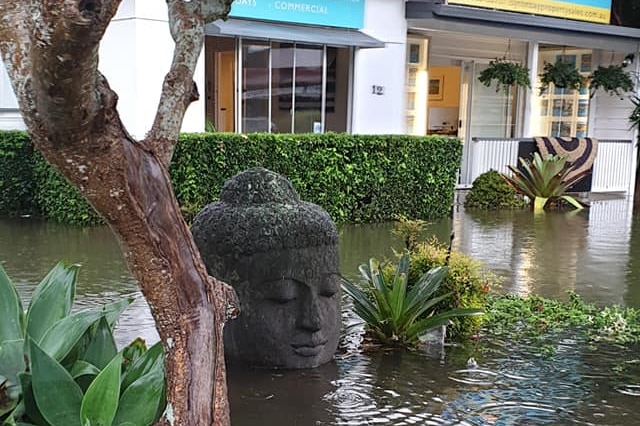 a buddha head above floodwaters in front of a real estate agent