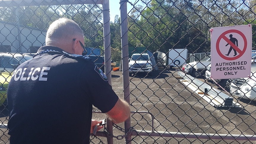 A police officer has back to camera using keys to open a gate, behind which is the allegedly stolen 4WD.