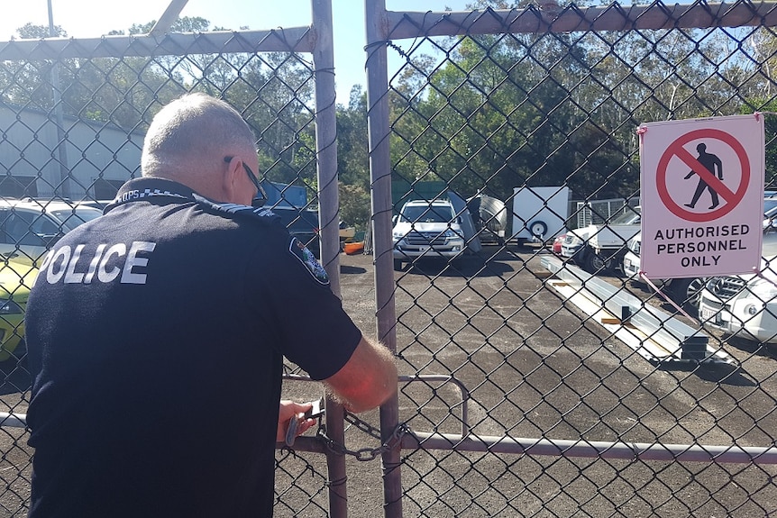 A police officer has back to camera using keys to open a gate, behind which is the allegedly stolen 4WD.