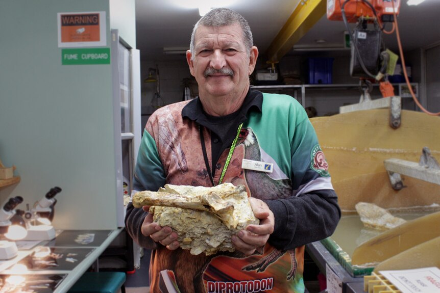 Alan Rackman holding a large fossil in limestone.