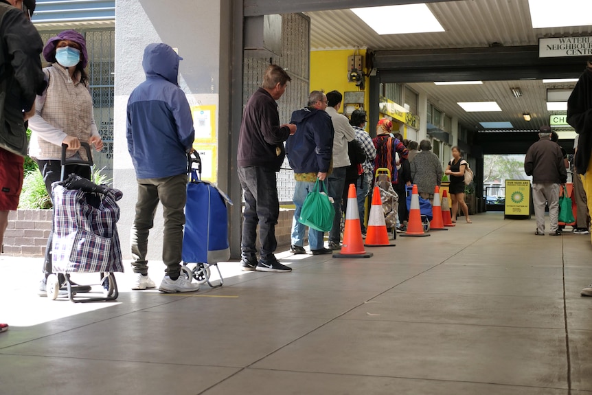 A line of twelve people queue in a covered supermarket
