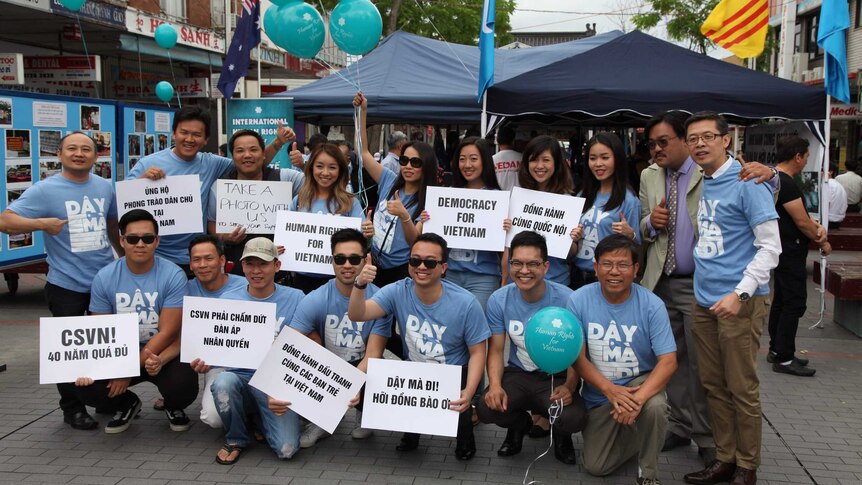 A group of people wearing matching blue shorts with blue balloons hold signs and smile for a photo.