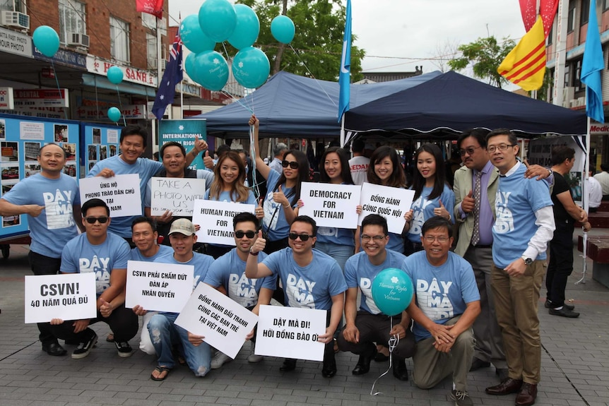 A group of people wearing matching blue shorts with blue balloons hold signs and smile for a photo.