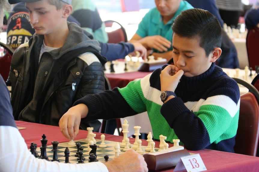 Boy moves piece during chess game.