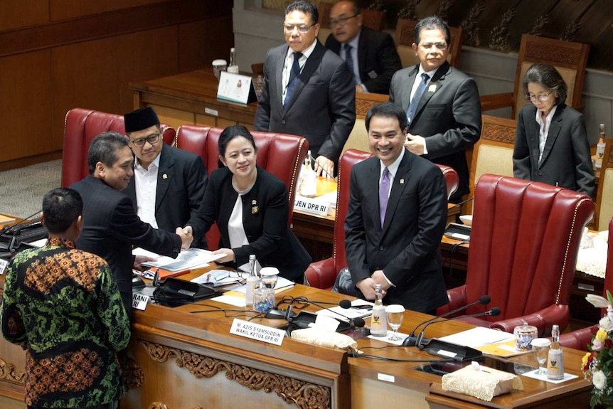 People stand in the Indonesian parliament smiling, while two shake hands.