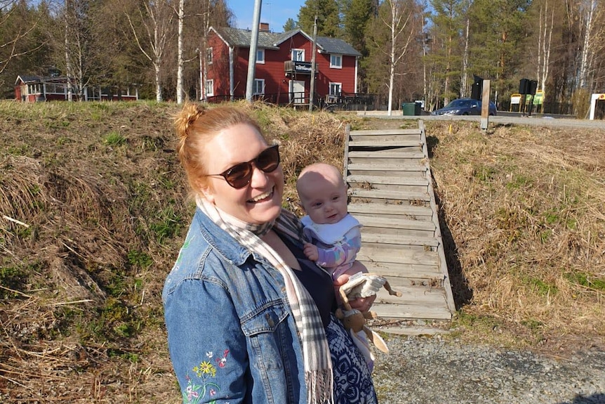 Wendy standing in the countryside while holding her baby daughter.