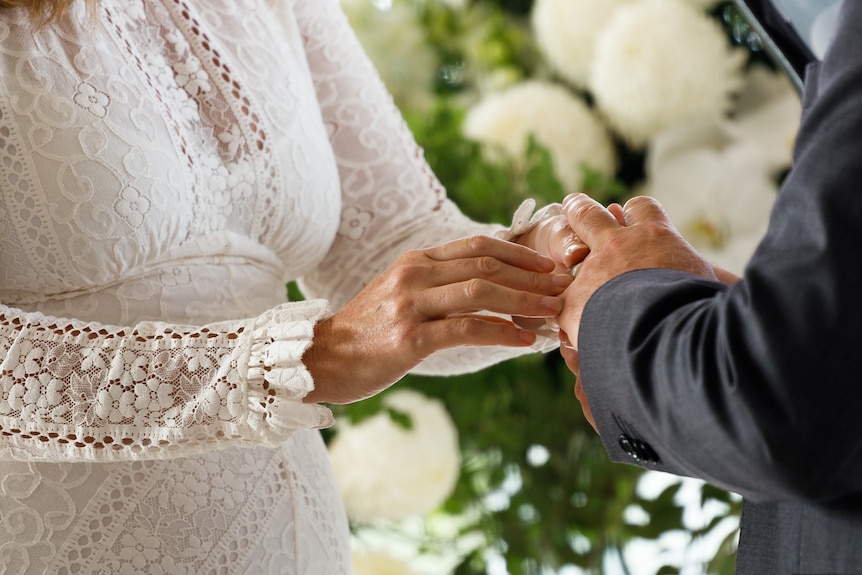 a woman's hand holding putting a ring on a man's finger