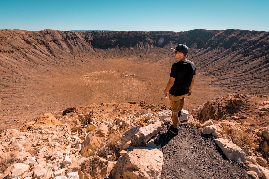 A man stands on the edge of a meteor crater.