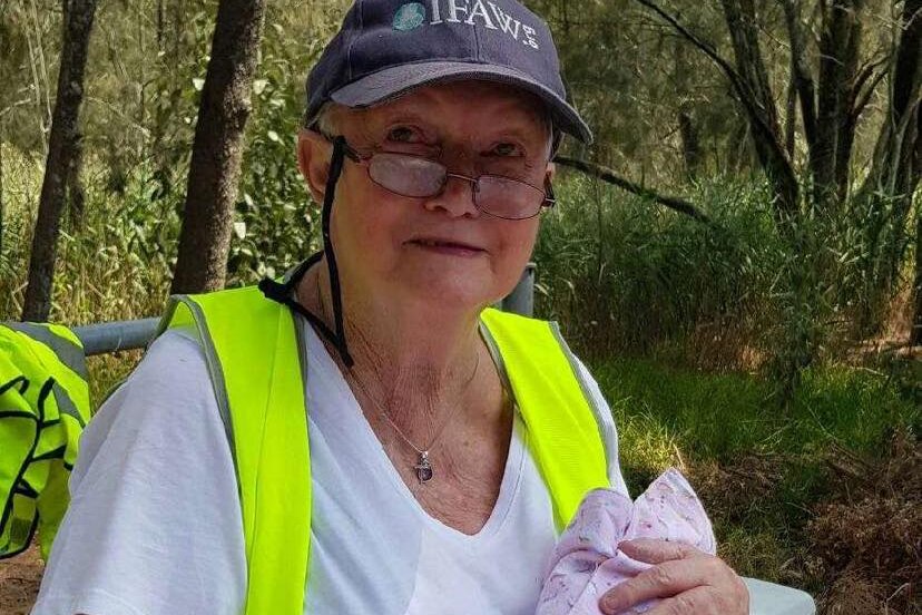 elderly woman with glasses in a white top and safety vest holds bundle of blankets