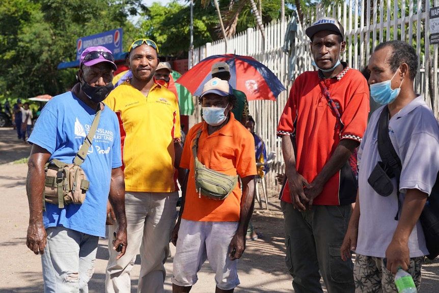 A group of men wearing masks with varying levels of success on a street in Port Moresby