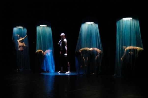 A dark stage with blue spotlights on dancers in poses.