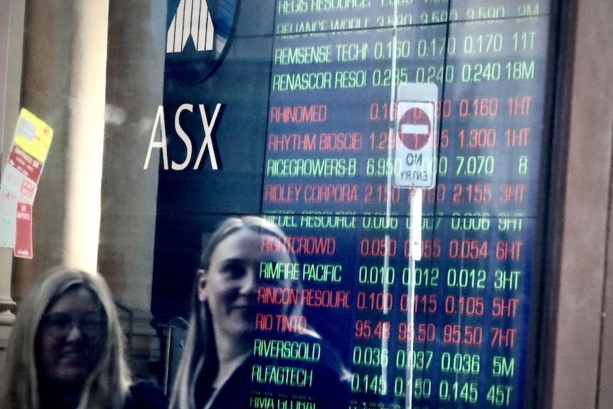 Two women look at a share price board outside the ASX in Sydney.