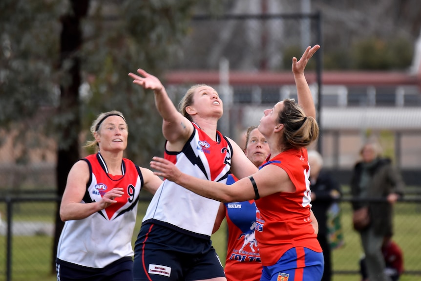 Two female Aussie Rules players have their hands up in the air as they jostle to win possession of the ball.